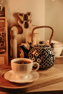 An inviting ceramic teapot with bright floral patterns, placed on a rustic wooden tray with a cup of tea.
