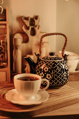 An inviting ceramic teapot with bright floral patterns, placed on a rustic wooden tray with a cup of tea.
