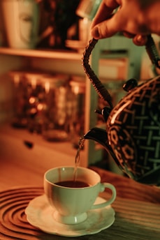 Elegant teapot pouring rich black tea into a porcelain cup with a backdrop of cozy café ambiance.