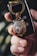 A close-up of a hand holding a set of car keys with a decorative keychain featuring an intricately detailed lion's head. The lion's head appears to be made of metal with a bronze and silver color finish, and is adorned with a rose design. The key fob is black with visible buttons and is secured by a gold-colored keyring.