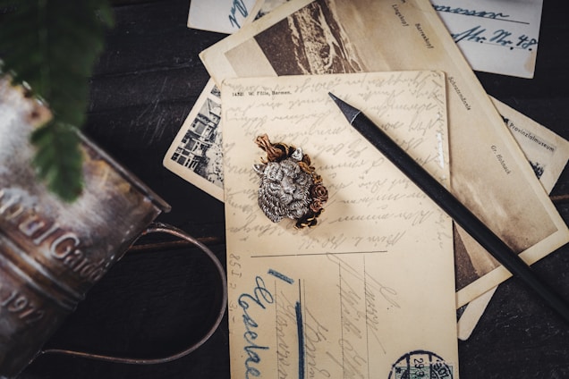 An arrangement of vintage postcards featuring handwritten messages, accompanied by a pencil and a decorative brooch. The scene is set on a dark wooden surface, adding a classic and nostalgic atmosphere.