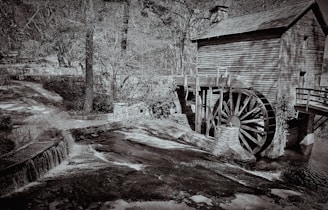 Historic water mill by a flowing stream surrounded by lush greenery.