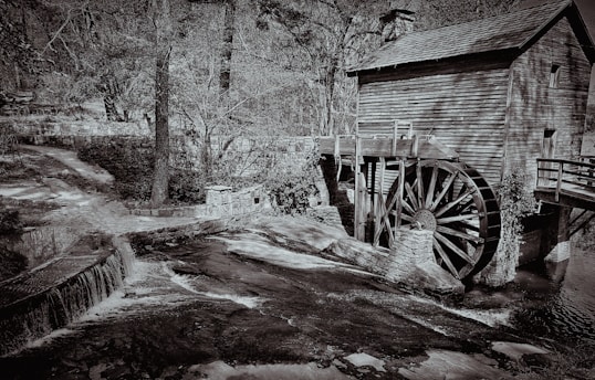 Historic water mill by a flowing stream surrounded by lush greenery.