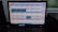 A computer monitor displays a software interface with multiple rectangular panels, each containing text and numerical data. The panels are organized in a grid format, aligned neatly across the screen. There are various icons and menus on the left and right sides of the screen indicating navigation options. The room reflects low ambient lighting, and the keyboard is visible in the foreground.