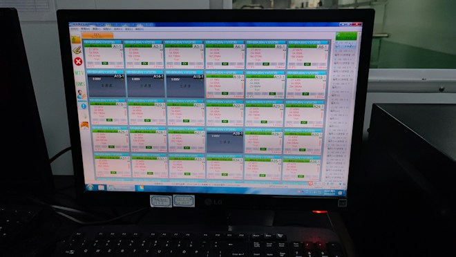 A computer monitor displays a software interface with multiple rectangular panels, each containing text and numerical data. The panels are organized in a grid format, aligned neatly across the screen. There are various icons and menus on the left and right sides of the screen indicating navigation options. The room reflects low ambient lighting, and the keyboard is visible in the foreground.