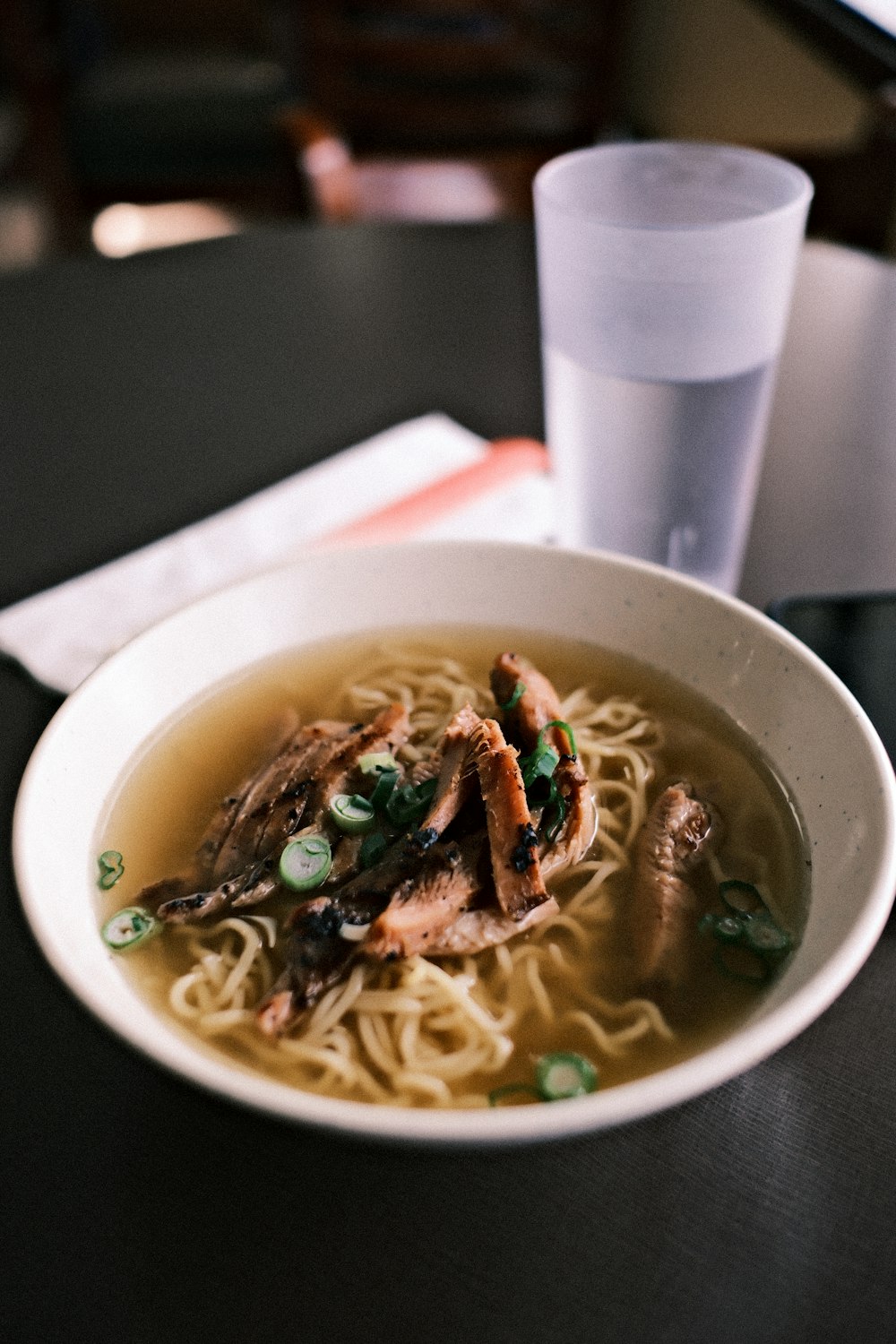 a bowl of noodles with meat and vegetables on a table