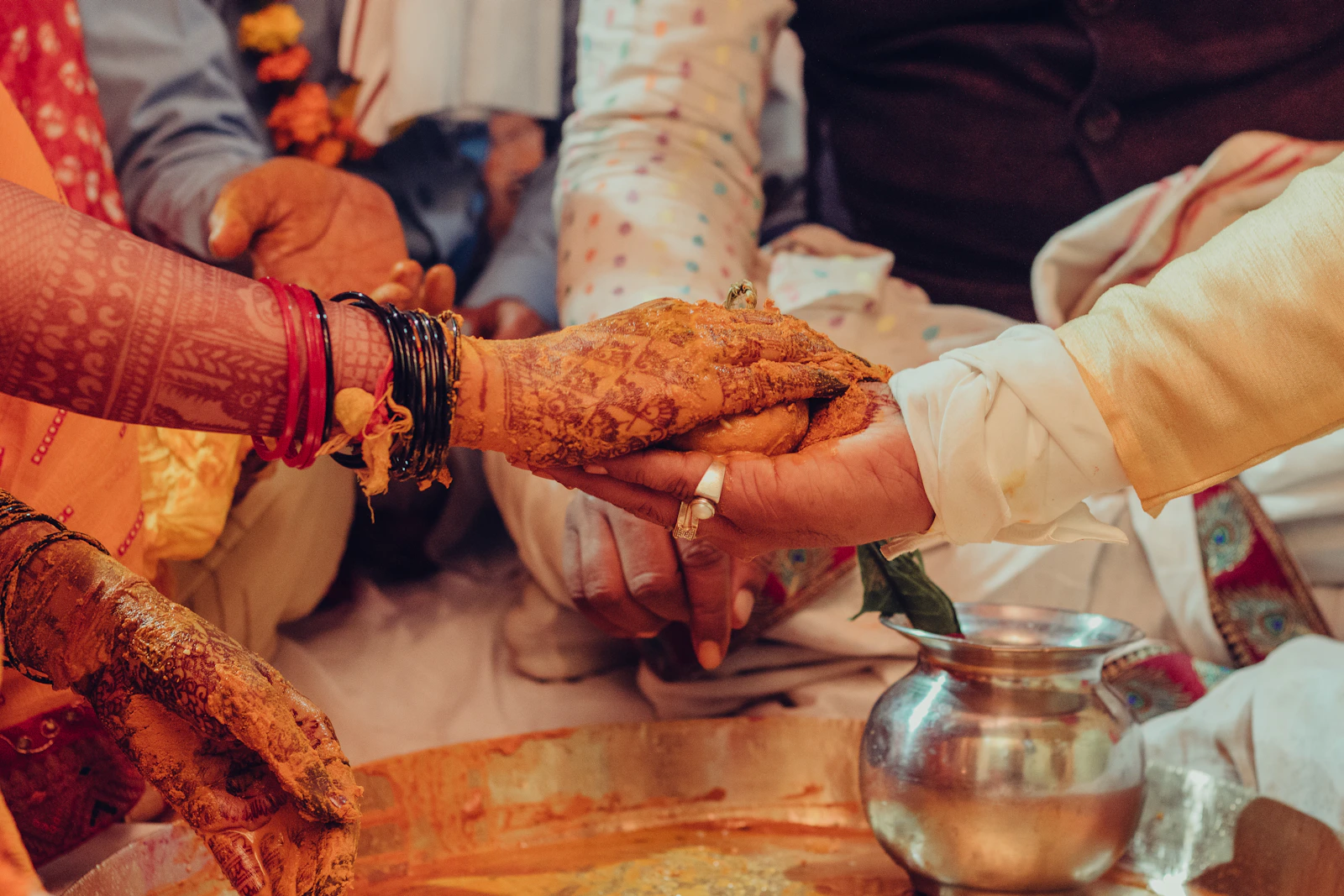 हल्दी लगे हाथों पर रखा वर का हाथ, पास में पीतल का कलश, विवाह की एक रस्म के दौरान।