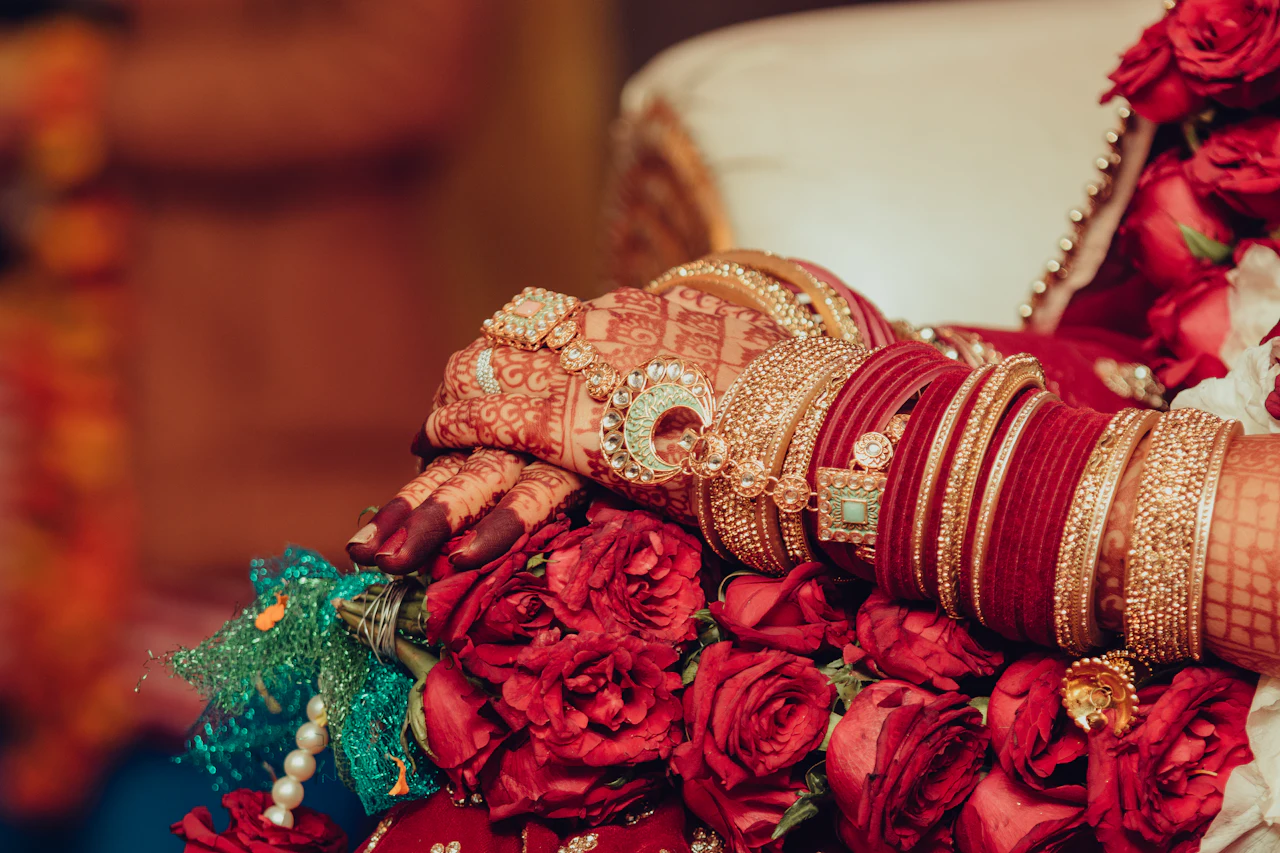 A bride’s hands with red bridal bangles and henna, holding a bouquet of red roses
