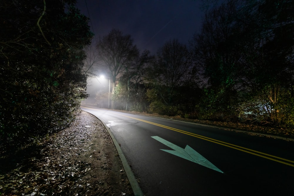 a street at night with a light on and an arrow painted on the road