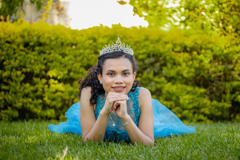 a young girl wearing a tiara laying in the grass