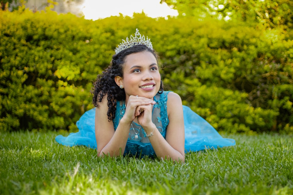 a woman laying on the grass wearing a tiara