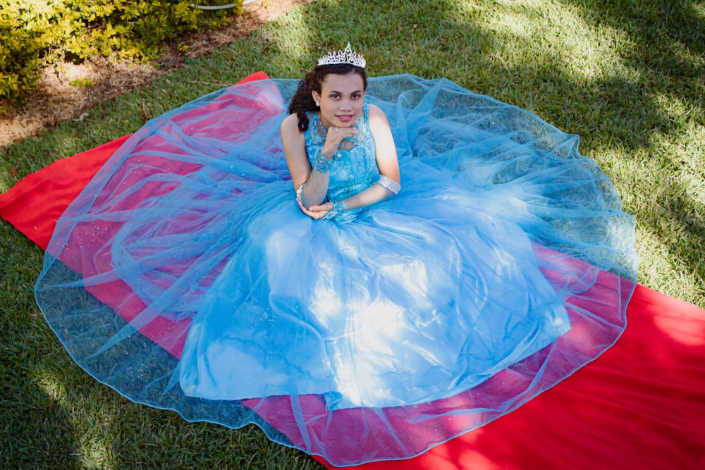 a woman in a blue and pink dress sitting on a red and blue blanket