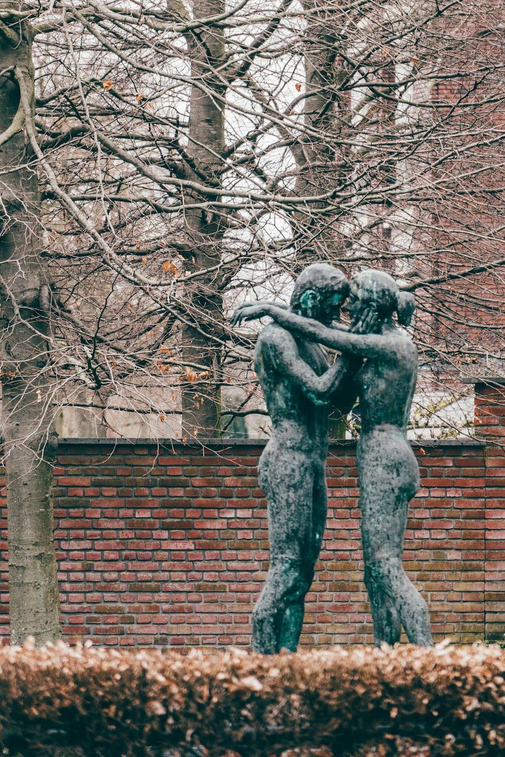 uma estátua de duas pessoas abraçando em frente a uma parede de tijolos