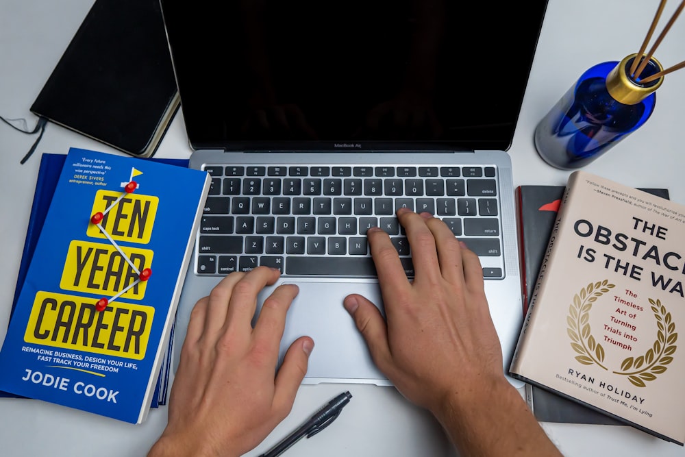 a person typing on a laptop next to a book