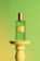 Close-up of a deep emerald green perfume bottle with metallic gold accents on a cream background.
