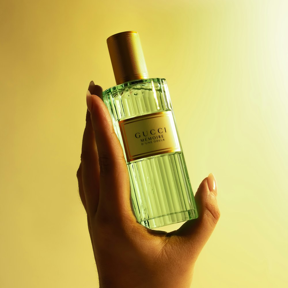 a hand holding a green bottle of perfume