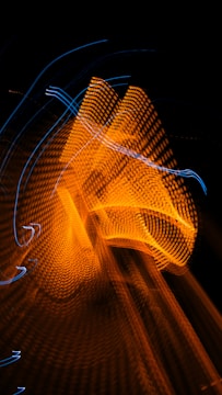 A dynamic abstract pattern of swirling orange and blue light trails against a dark background, creating a sense of motion and energy.