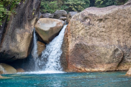 A cascading waterfall flowing over natural stones into a crystal-clear pool.