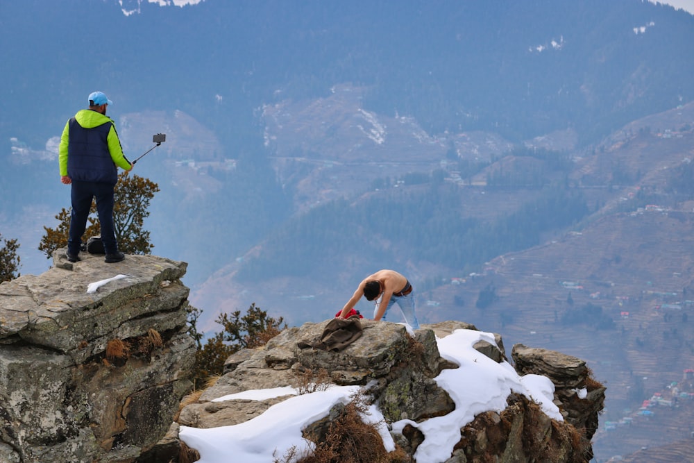 Un homme debout au sommet d’une montagne à côté de rochers enneigés