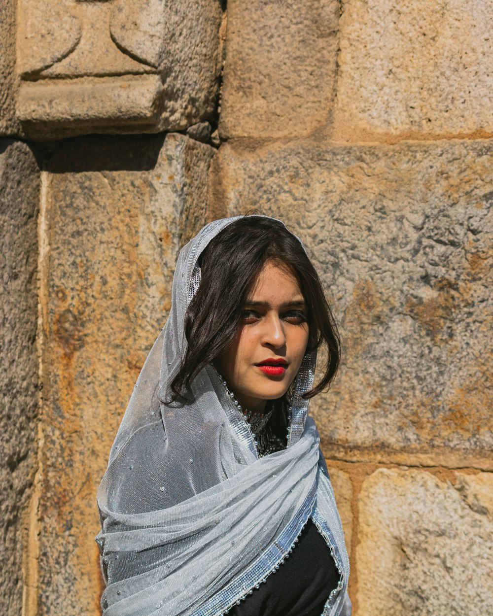 a woman with a veil on her head standing in front of a stone wall