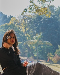 A serene woman sitting outdoors with a journal, sunlight filtering through trees.
