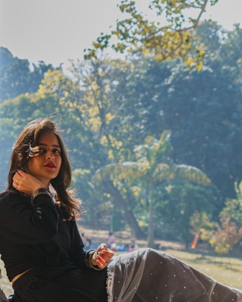 A serene woman sitting outdoors with a journal, sunlight filtering through trees.