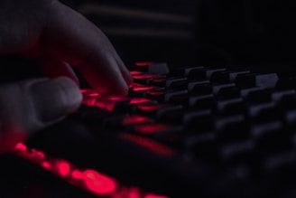 Close-up of a hacker’s hands typing code with dark red lighting highlighting the scene.