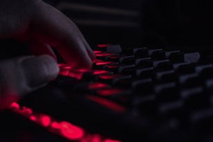 Close-up of a hacker’s hands typing code with dark red lighting highlighting the scene.