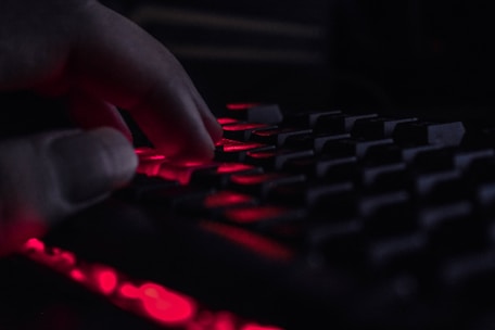 A close-up of hands typing on a keyboard with a glowing monitor in the background.