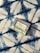 A bar of natural soap in a package lies on a patterned fabric surface. The soap packaging displays text and nature-related symbols, suggesting it is an organic product. The fabric features a bold, abstract blue and white pattern with a textured appearance.