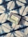 A bar of natural soap in a package lies on a patterned fabric surface. The soap packaging displays text and nature-related symbols, suggesting it is an organic product. The fabric features a bold, abstract blue and white pattern with a textured appearance.