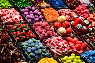 An assortment of colorful candy displayed in clear containers, featuring a variety of shapes and textures. The selection includes sweets that resemble berries, citrus slices, and marshmallows, arranged in an eye-catching, organized layout.