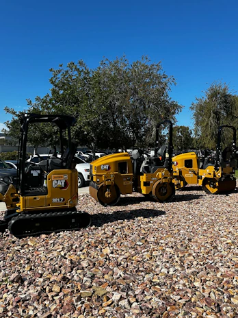 A row of heavy construction machines ready for rental at a sunny outdoor yard.