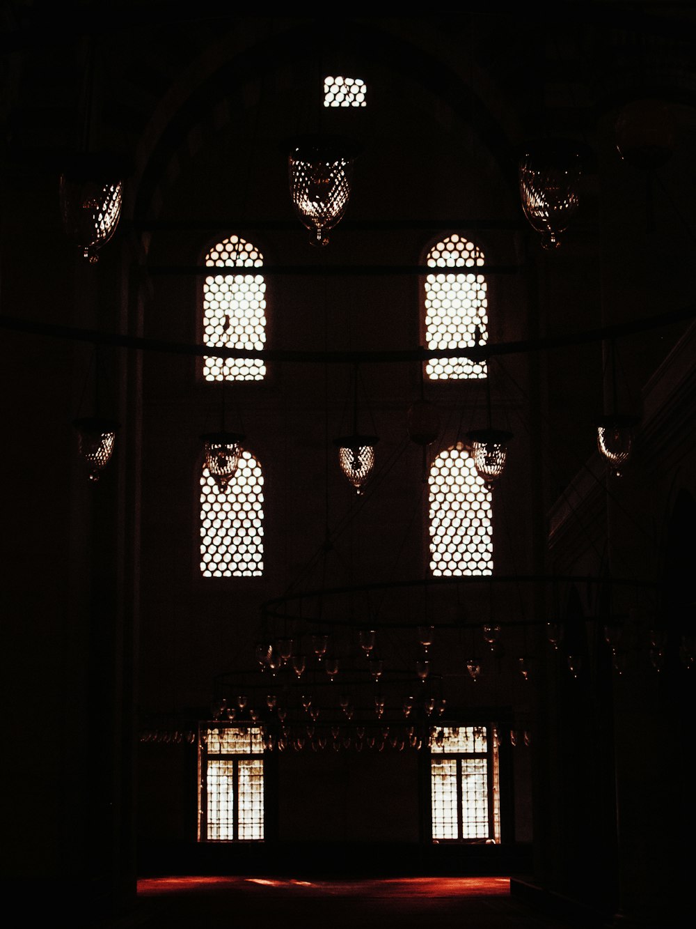 a dark room with four windows and a chandelier hanging from the ceiling