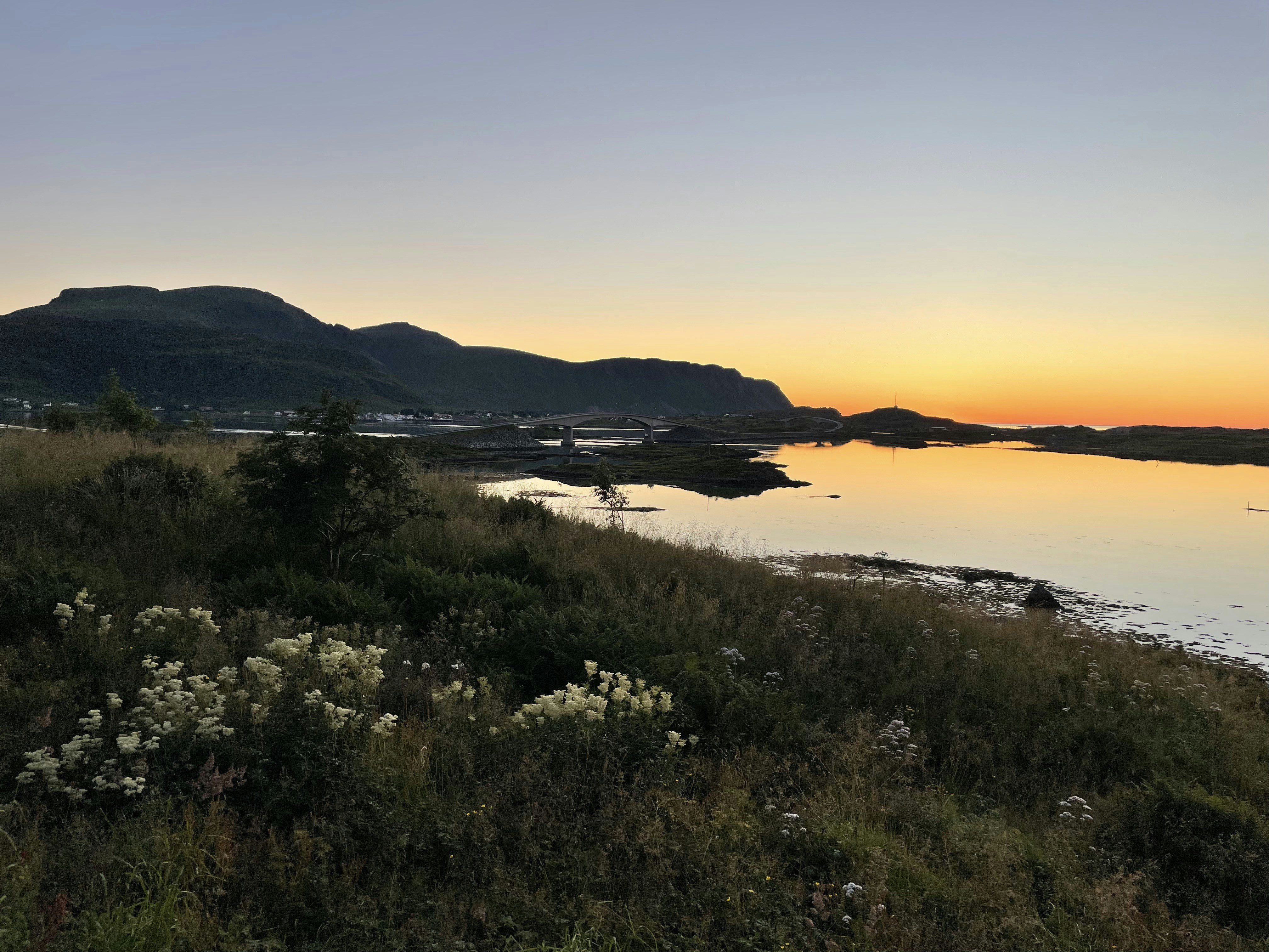 The sun is setting over a body of water, sunset with mountain in background