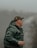 Close-up of a hunter wearing a camo Delta Creek cap, standing in mist over a pond at sunrise.