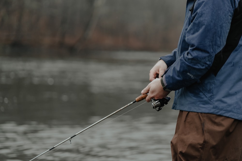a man holding a fishing rod while standing next to a body of water