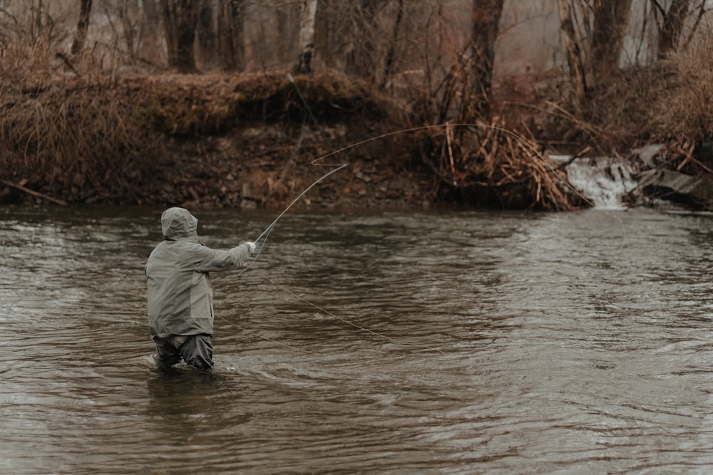 a man standing in a river while holding a fishing rod