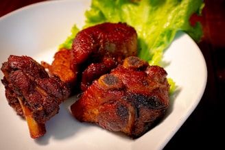 Juicy, cooked pieces of pork are arranged on a white plate, accompanied by fresh green lettuce leaves. The meat appears well-cooked with a dark, caramelized crust, suggesting thorough roasting or grilling.