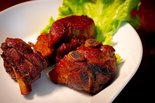 Juicy, cooked pieces of pork are arranged on a white plate, accompanied by fresh green lettuce leaves. The meat appears well-cooked with a dark, caramelized crust, suggesting thorough roasting or grilling.