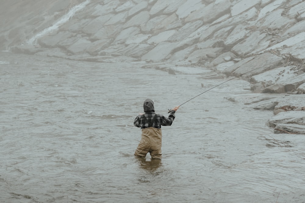 a man standing in a river while holding a fishing pole