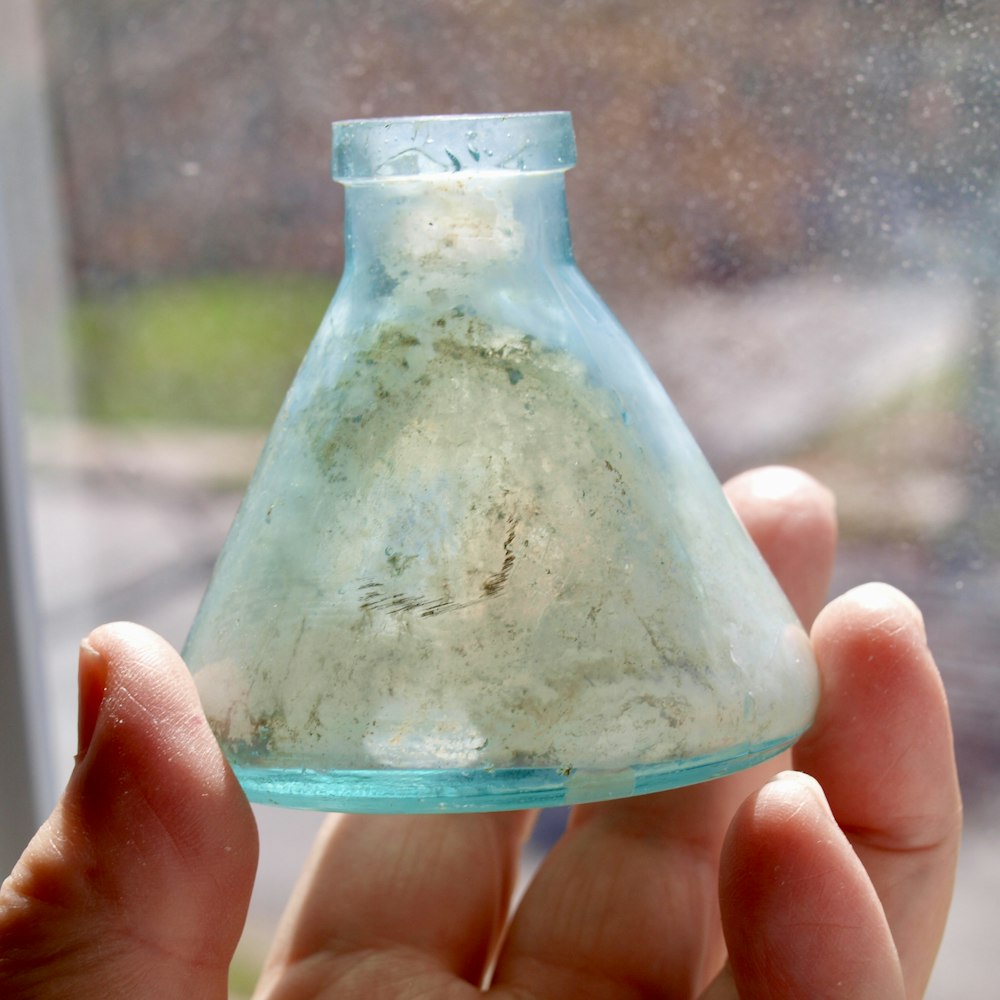 a hand holding a small glass vase with dirt inside of it
