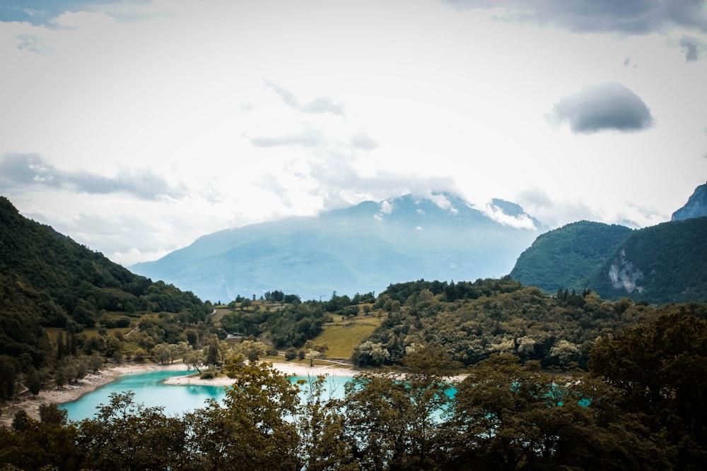 a lake surrounded by trees and mountains under a cloudy sky