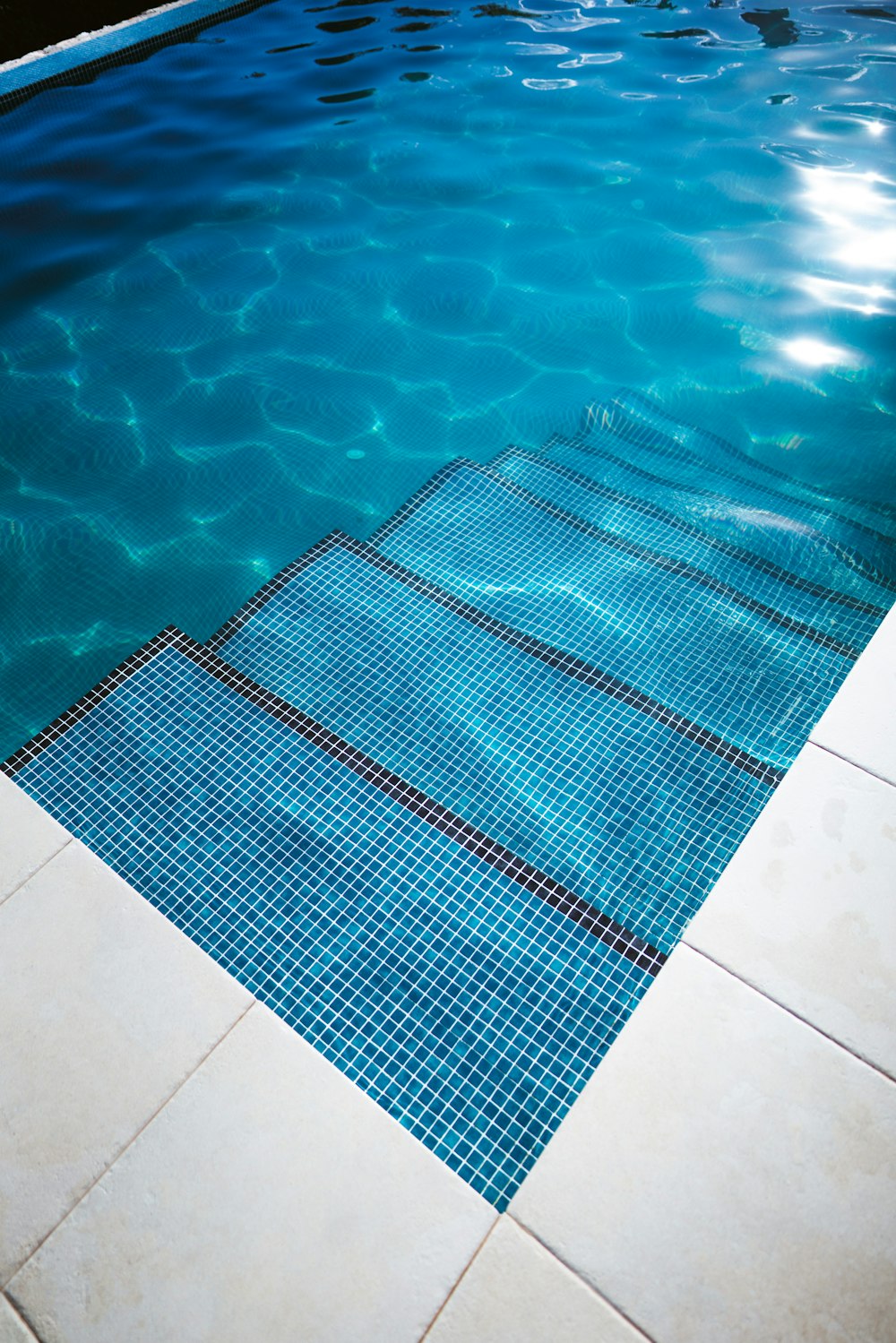 a blue swimming pool with a white tiled floor