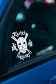 A car window features a decal depicting a hockey mask centered between crossed chopsticks. The words 'Ramen Riders' are displayed, with some characters in an Asian script.