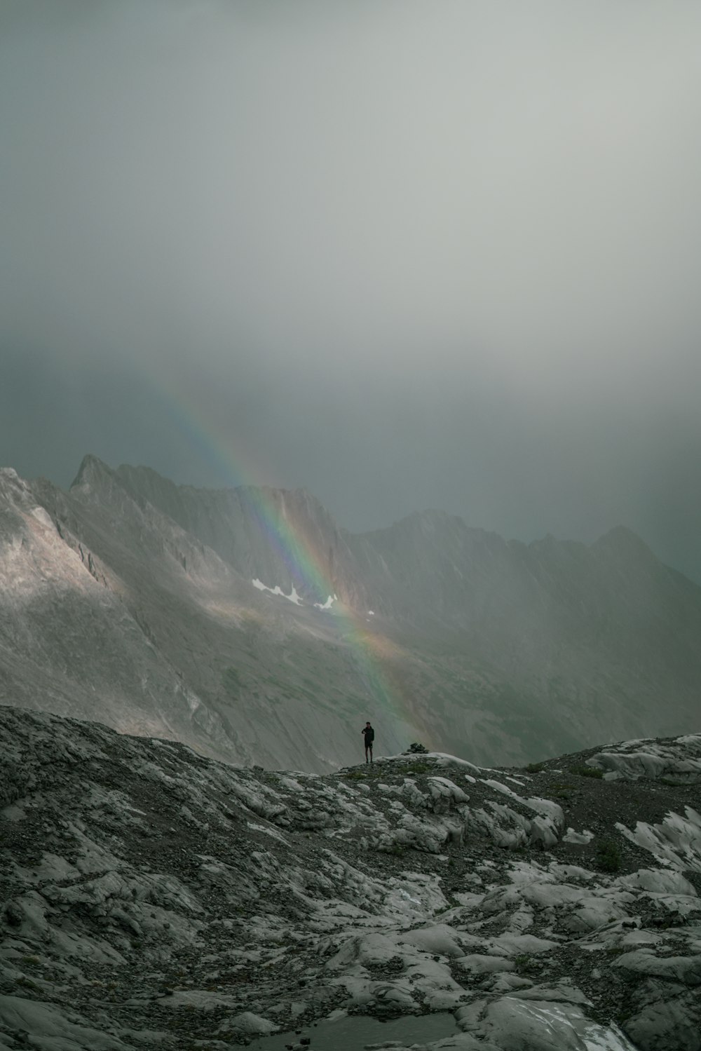 a person standing on top of a mountain under a rainbow