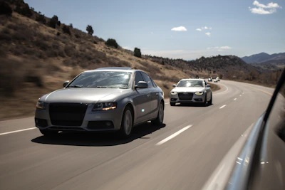 A convoy of car carriers moving through a scenic mountain pass under clear skies.