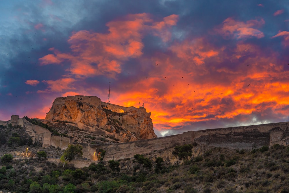 a sunset view of a rocky mountain with birds flying in the sky