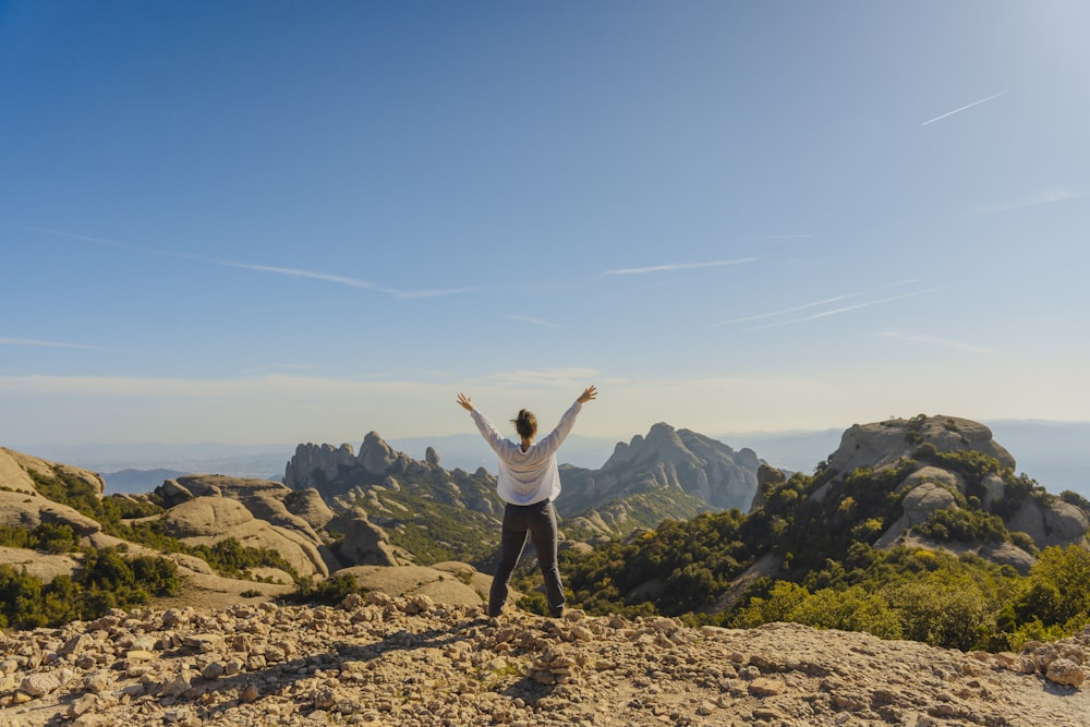 uma pessoa de pé no topo de uma montanha com os braços no ar