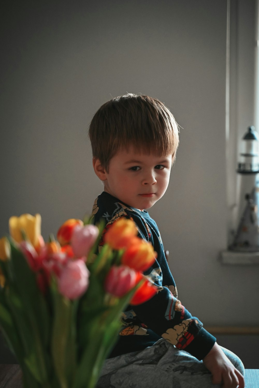 a young boy sitting on a table with a vase of tulips
